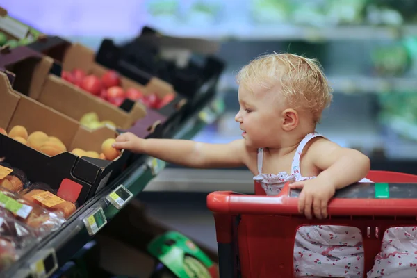 Bebé niña recogiendo albaricoque de una caja en el estante —  Fotos de Stock