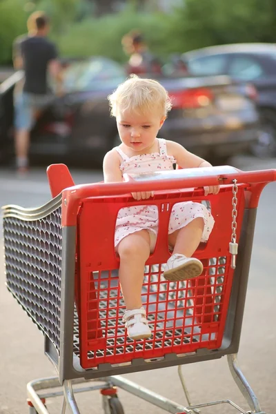 Bambina seduta nel carrello della spesa rosso — Foto Stock