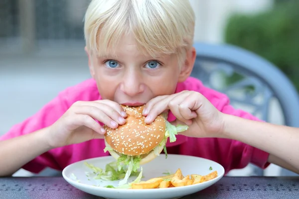 Ragazzo adolescente mangiare hamburger con insalata — Foto Stock