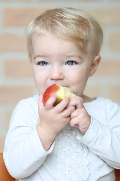 Baby girl bites on tasty red apple — Stock Photo, Image