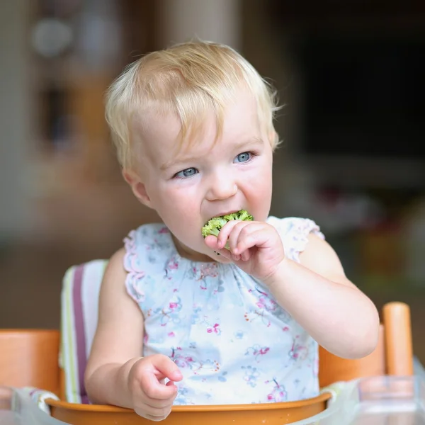 Baby girl biting on broccoli — Stock Photo, Image