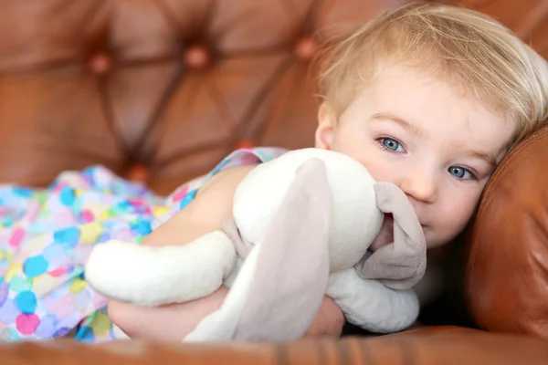 Girl lying on sofa holding rabbit toy — Stock Photo, Image