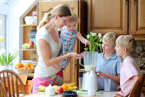 Mother with three kids preparing healthy drink with milk and fruits — Stock Photo, Image