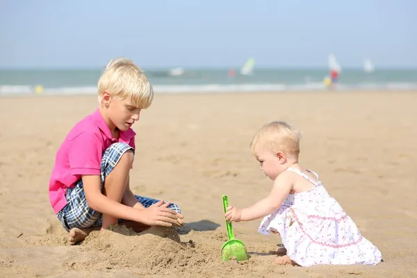 Jongen en zijn kleine zusje spelen samen op het strand — Stockfoto