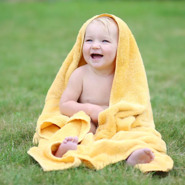 Baby sitting on green grass in warm yellow towel — Stock Photo, Image