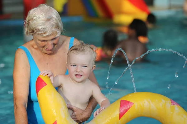 Orgogliosa donna anziana sana sta godendo il tempo con il suo adorabile nipote di un anno in una piscina — Foto Stock