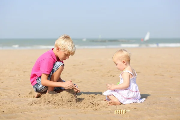 Pojken och hans lilla lillasyster spelar tillsammans på stranden — Stockfoto