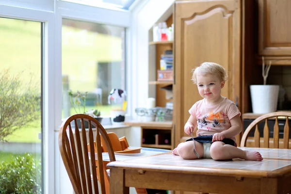 Meisje eten iets met vork zittend op de tafel — Stockfoto