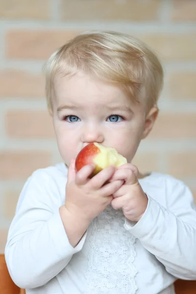 Baby girl bites on tasty red apple — Stock Photo, Image