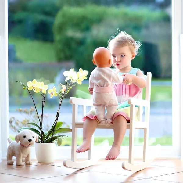 Dziewczyna bawi sie z lalka siedzi na krześle — Zdjęcie stockowe