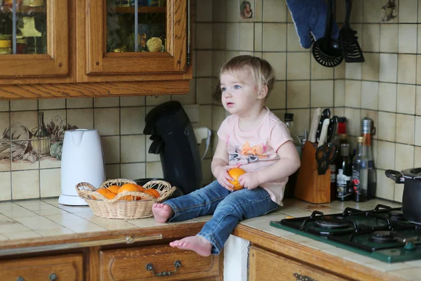 Girl sitting on the working surface holding orange — Stock Photo, Image