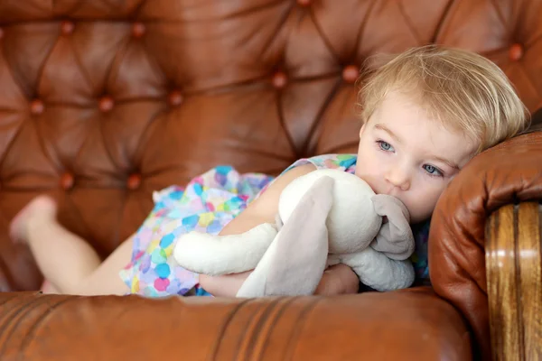 Menina deitada no sofá segurando brinquedo de coelho — Fotografia de Stock