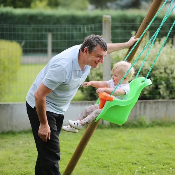 Buon padre con la sua adorabile bambina che gioca con l'altalena in giardino nel cortile della casa — Foto Stock