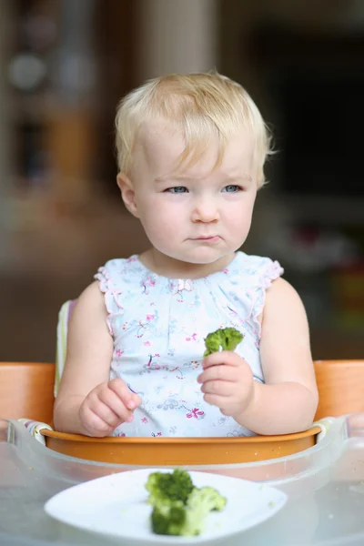 Baby girl eating steamed broccoli
