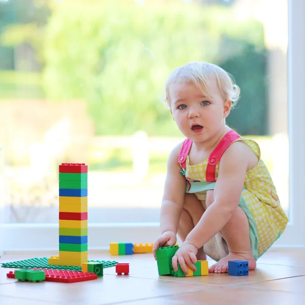 Chica jugando con bloques de plástico sentado en el suelo de baldosas —  Fotos de Stock