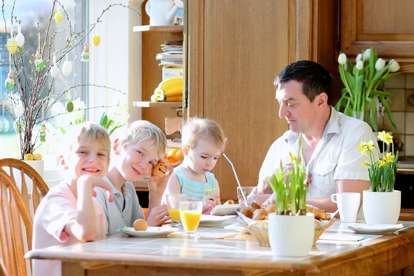 Vader met drie kinderen, zonen tiener en peuter dochter eieren eten tijdens het familie Ontbijt op Pasen dag zitten samen in zonnige keuken. selectieve aandacht op meisje. — Stockfoto