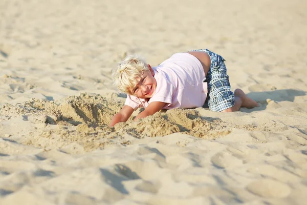 Мальчик копает большую яму в песке на пляже — стоковое фото