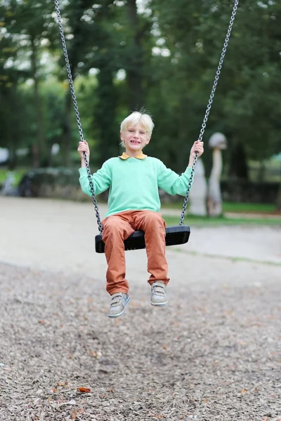 Menino se divertindo balançando no playground — Fotografia de Stock