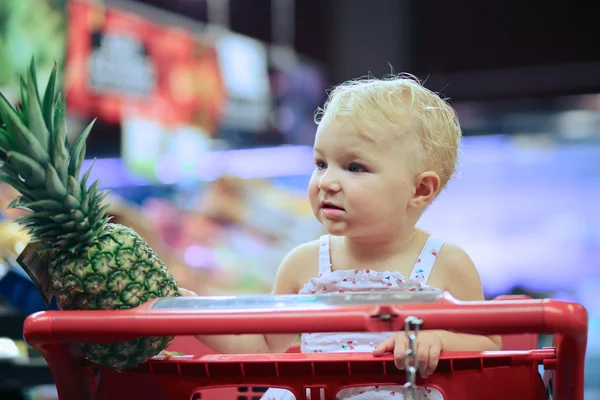 Süpermarkette kırmızı alışveriş sepeti oturuyor ve bebek kız — Stok fotoğraf