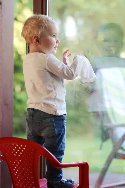 Baby girl cleaning window door with wet serviette — Stock Photo, Image