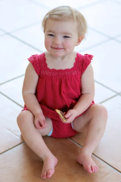Dziewczynka jedzenie cookie siedzący przytulne, na podłodze płytki — Zdjęcie stockowe