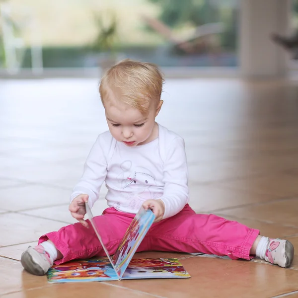 Bebê menina leitura livro sentado dentro de casa — Fotografia de Stock