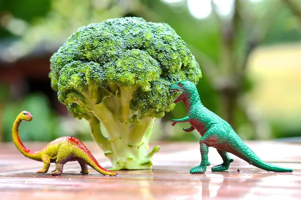 Funny picture of toy dinosaur eating broccoli tree. Photo can be used to help cooking with children, preparing kid-friendly dishes and promoting healthy food for children — Stock Photo, Image