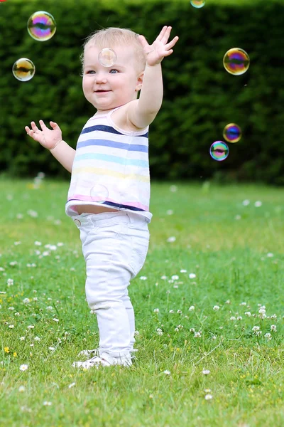 Girl is playing outdoors trying to catch soap bubbles Royalty Free Stock Images