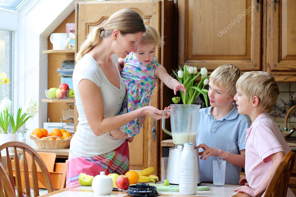 Mother with three kids preparing healthy drink with milk and fruits