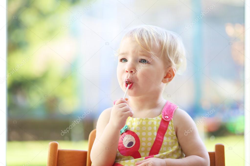 Girl eating lollipop sitting in the kitchen