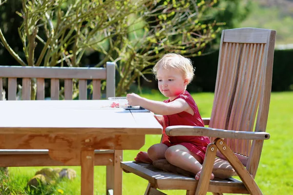 Cute little girl eating berries sitting at picnic table in the garden — Stock Photo, Image