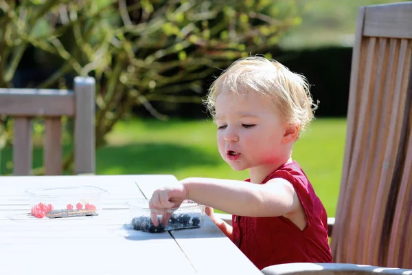 Cute little girl eating berries sitting at picnic table in the garden — Stock Photo, Image