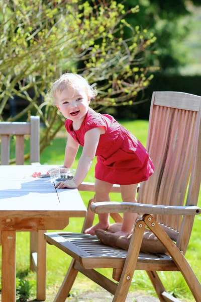 Счастливая малышка играет в саду, сидя за деревянным столом для пикника — стоковое фото