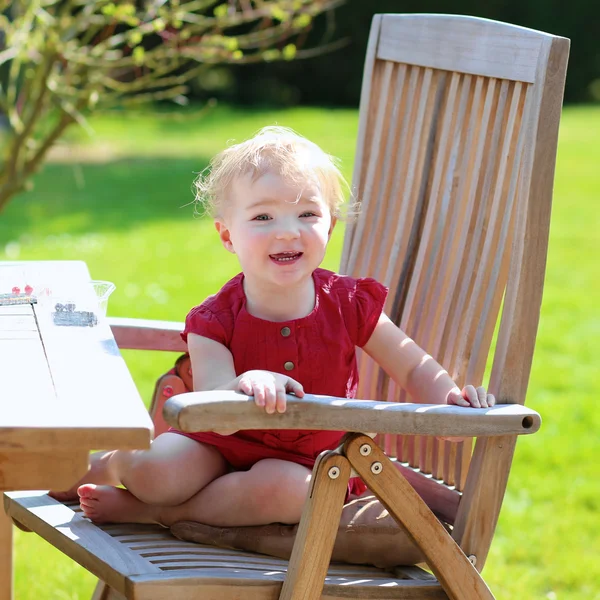 Ευχαρίστως toddler κορίτσι παιχνίδι στον κήπο κάθεται στο ξύλινο τραπέζι πικνίκ — Φωτογραφία Αρχείου