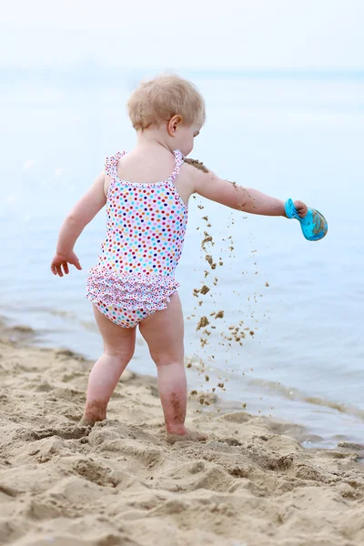Счастливая маленькая девочка в купальнике играет на песчаном пляже — стоковое фото