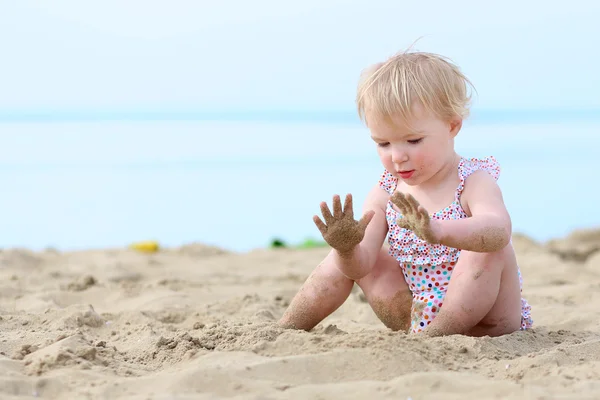 Happy little girl in spotty swimsuit playing on sandy beach — Stock Photo, Image