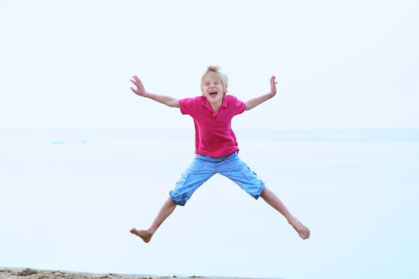 Felice ragazzo adolescente attivo divertirsi saltando sulla spiaggia — Foto Stock