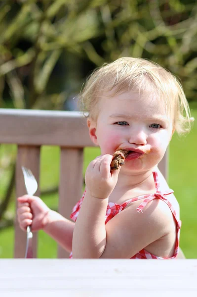 屋外グリルしたお肉を食べて幸せな幼児の女の子 — ストック写真