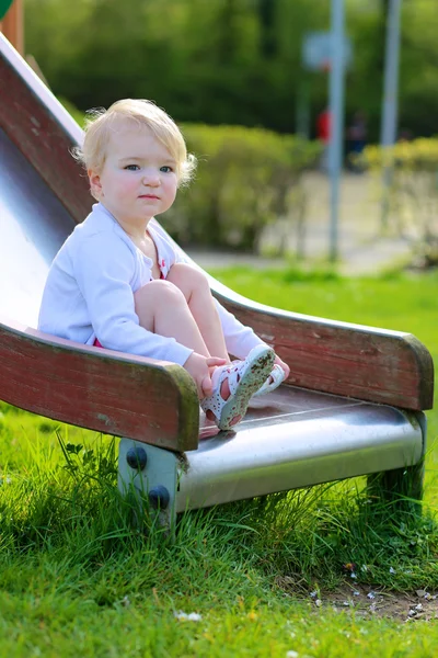 Cute girl relaxing on playground sitting on slide — Stock Photo, Image