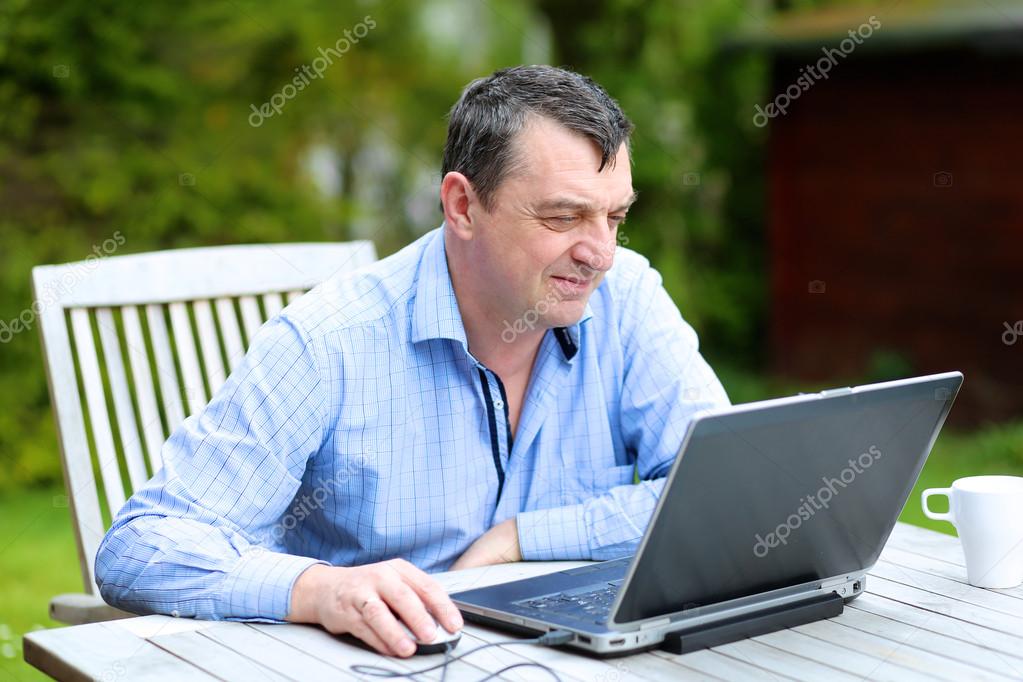 Businessman working from home sitting with laptop outside in the garden