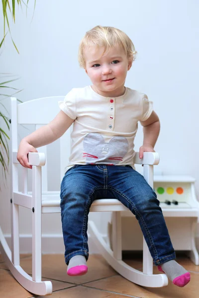 Retrato de un niño feliz con ropa casual posando en el interior de una mecedora blanca —  Fotos de Stock