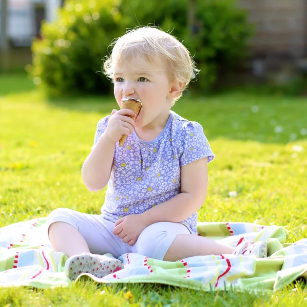 Felice carino sorridente bambino ragazza mangiare gelato seduto nel giardino estivo — Foto Stock