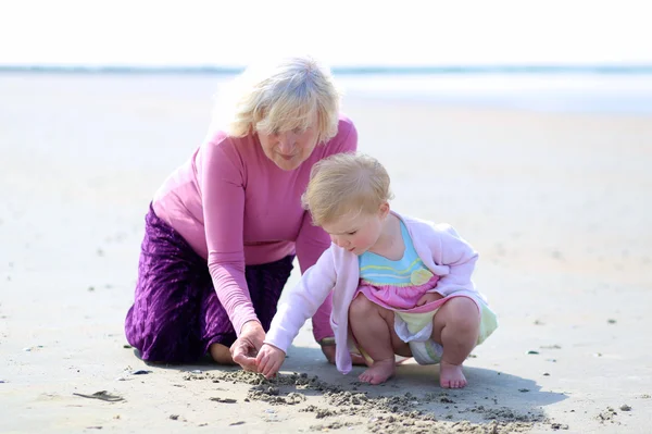 Happy grandmother playing with her granddaughter on the beach — Stock Photo, Image