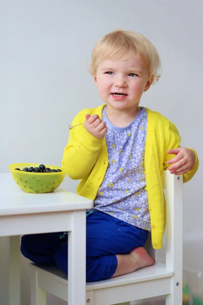Menina bonito comer mirtilos dentro de casa — Fotografia de Stock