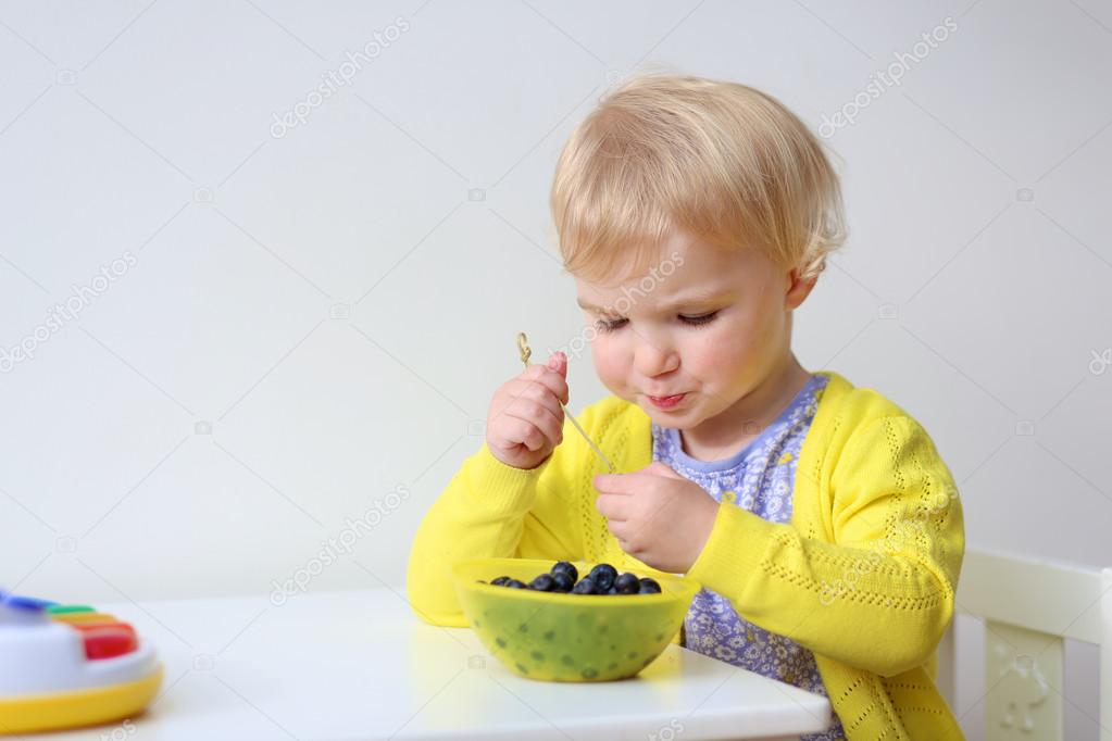 Cute little girl eating blueberries indoors