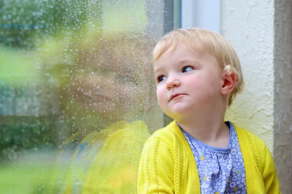 Petite fille mignonne regardant par la fenêtre pluvieuse — Photo
