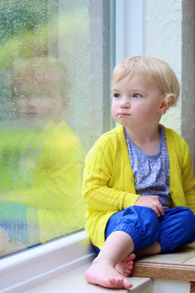 Söt liten flicka tittar ut regnigt fönster — Stockfoto