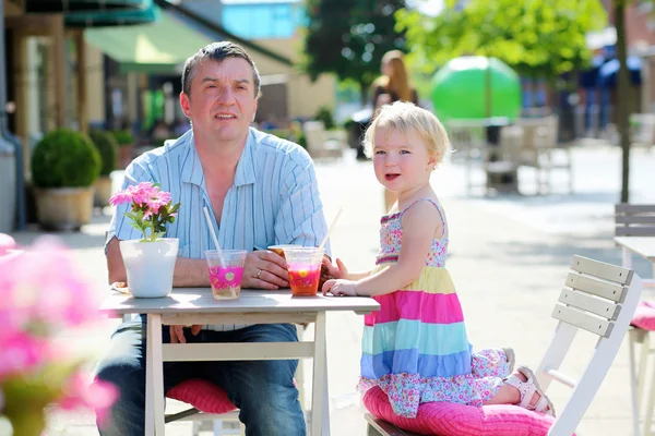 Father and little daughter drinking and eating in outdoors cafe — Stock Photo, Image