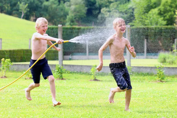 Два счастливых мальчика играют в саду из поливающего шланга — стоковое фото