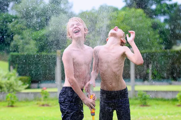Dva šťastné kluci hrají na zahradě s zavlažovací hadice — Stock fotografie